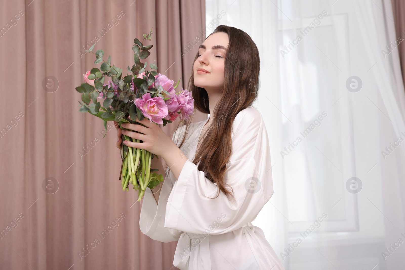 Photo of Beautiful young woman with bouquet of flowers indoors