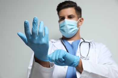 Photo of Doctor in protective mask and medical gloves against light grey background, focus on hands