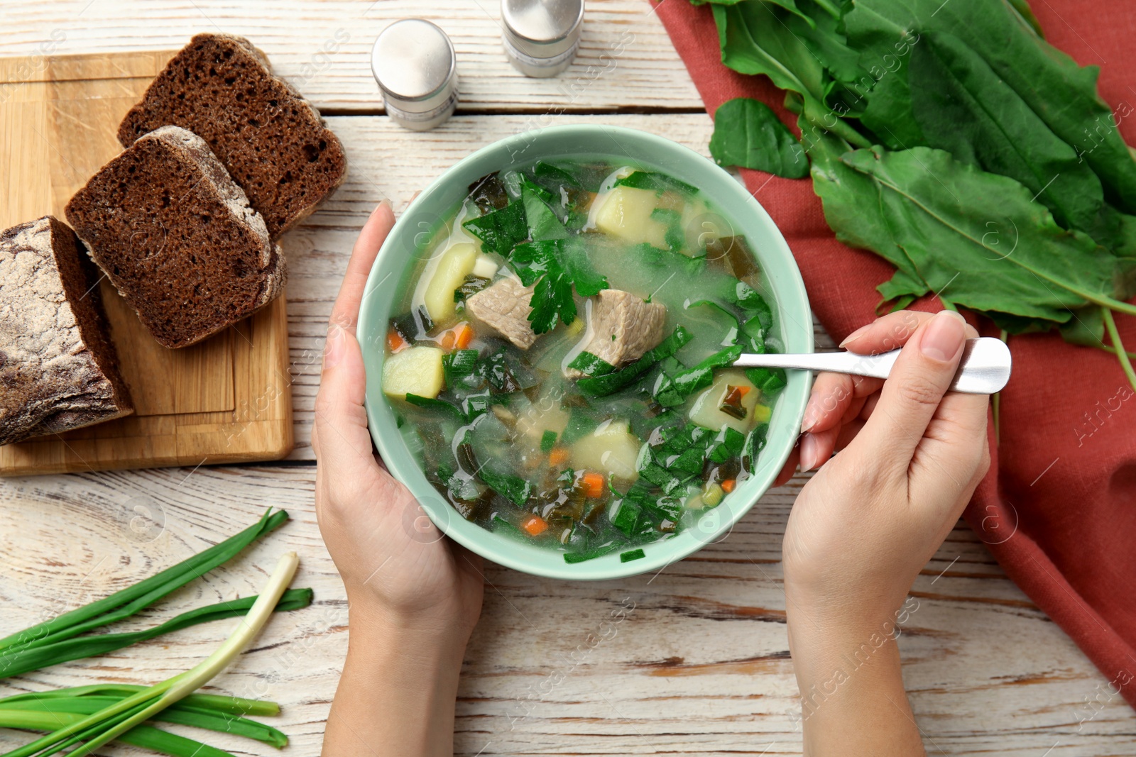 Photo of Woman eating delicious sorrel soup with meat at wooden table, top view