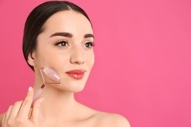 Woman using natural face roller on pink background, space for text