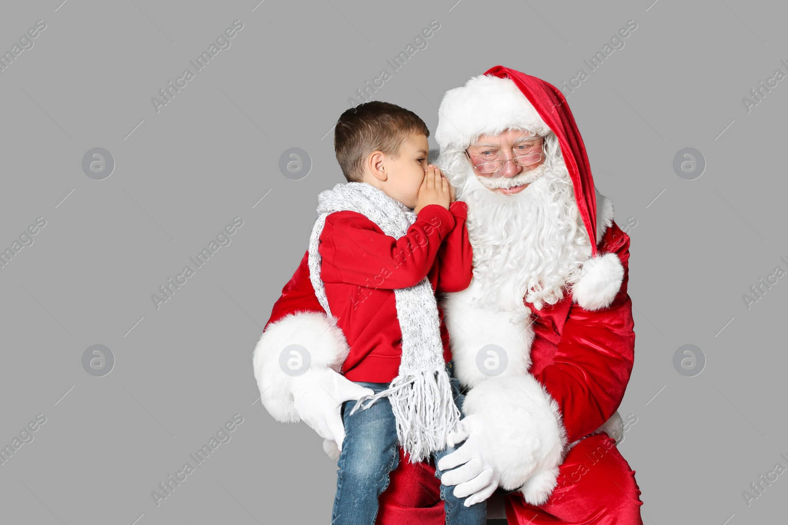 Photo of Little boy whispering in authentic Santa Claus' ear on grey background