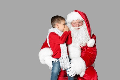 Photo of Little boy whispering in authentic Santa Claus' ear on grey background