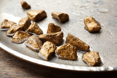 Photo of Plate with gold nuggets and water on table, closeup