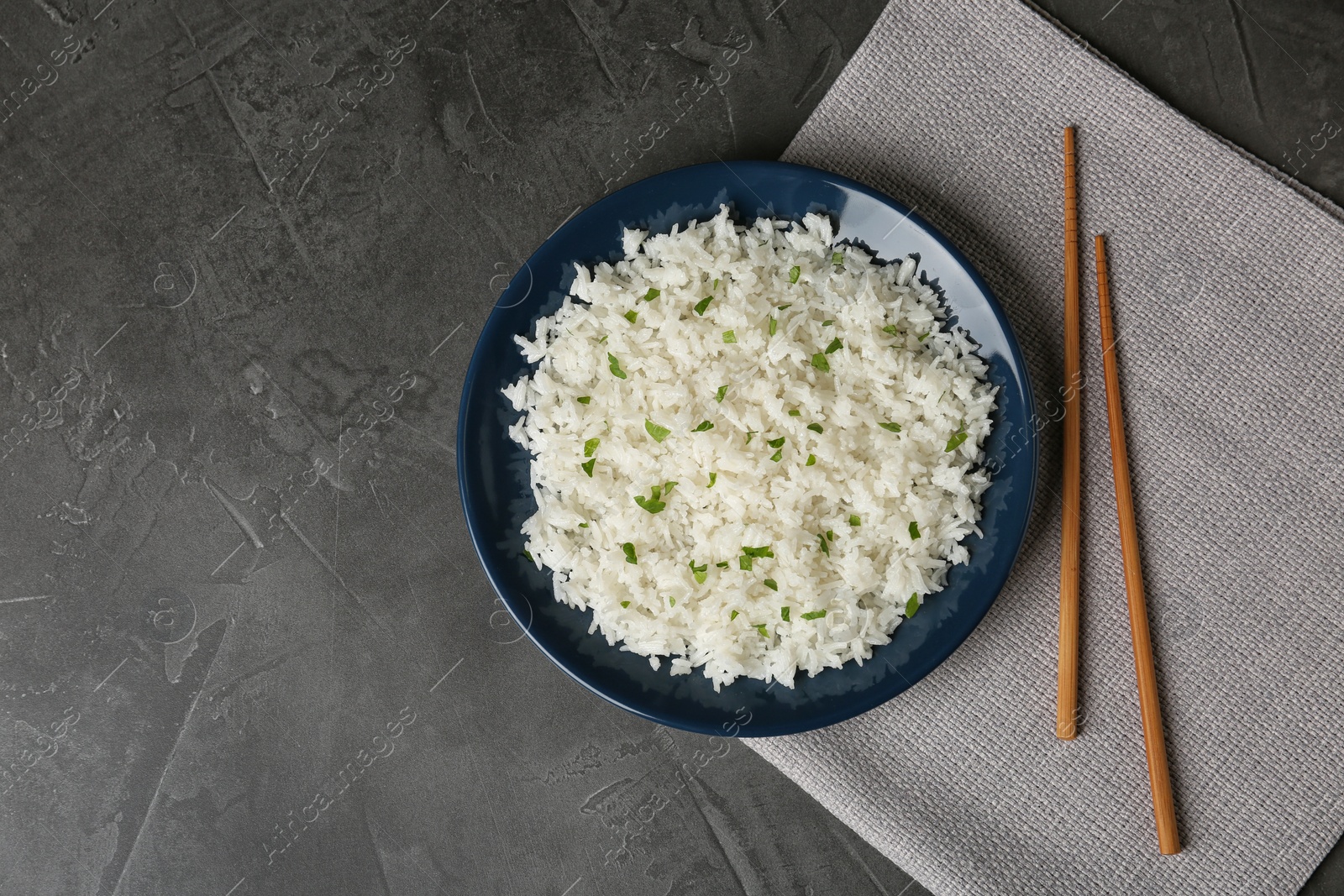 Photo of Plate of boiled rice and chopsticks on grey background, top view with space for text