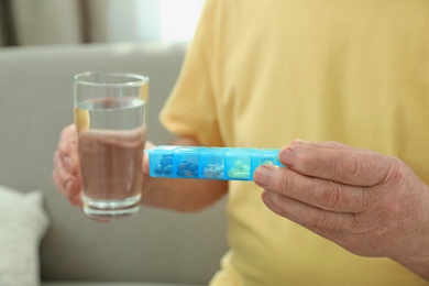 Elderly man with pills and glass of water in nursing home, closeup. Assisting senior people