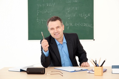 Male teacher working at table in classroom