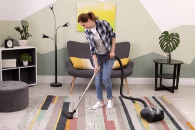 Photo of Woman removing dirt from carpet with vacuum cleaner at home