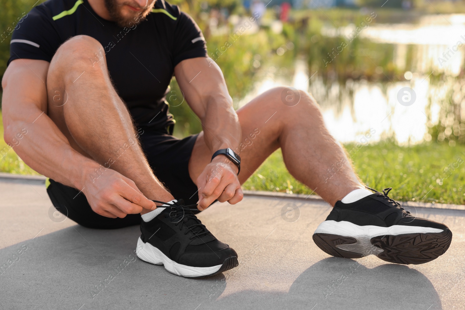 Photo of Man tying shoelaces before running outdoors on sunny day, closeup