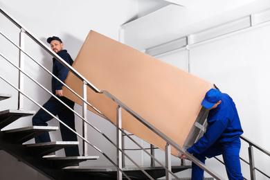 Professional workers carrying refrigerator on stairs indoors