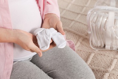 Pregnant woman with baby socks sitting on bed, closeup. Packing stuff for maternity hospital