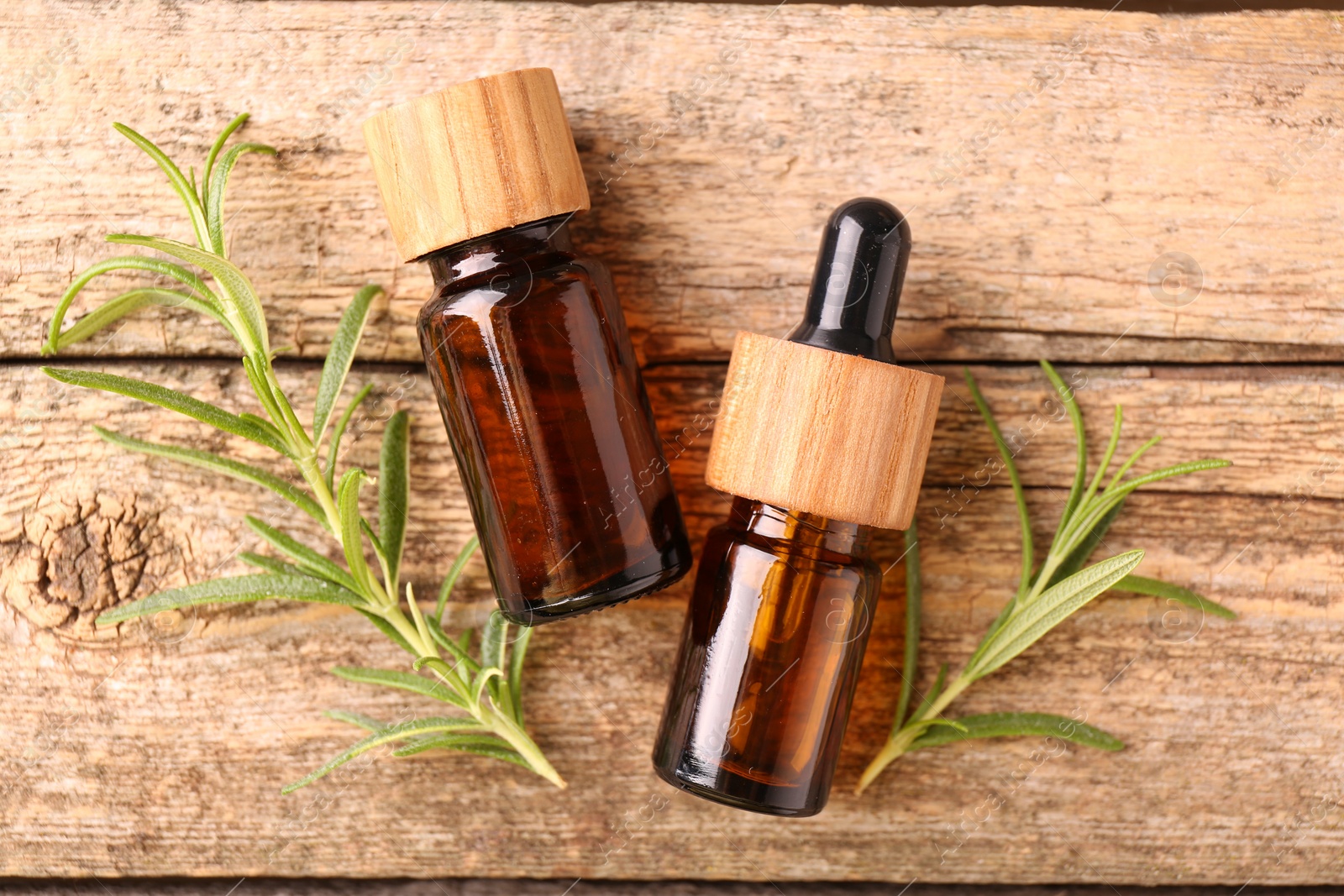 Photo of Aromatic essential oils in bottles and rosemary on wooden table, flat lay