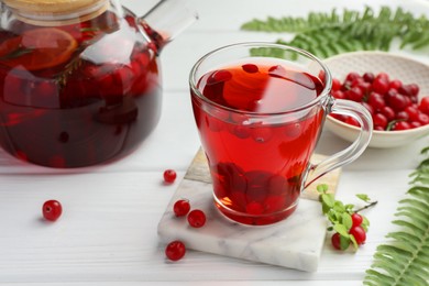 Photo of Tasty hot cranberry tea in glass cup, fresh berries and leaves on white wooden table