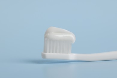 Photo of Plastic toothbrush with paste on light blue background, closeup