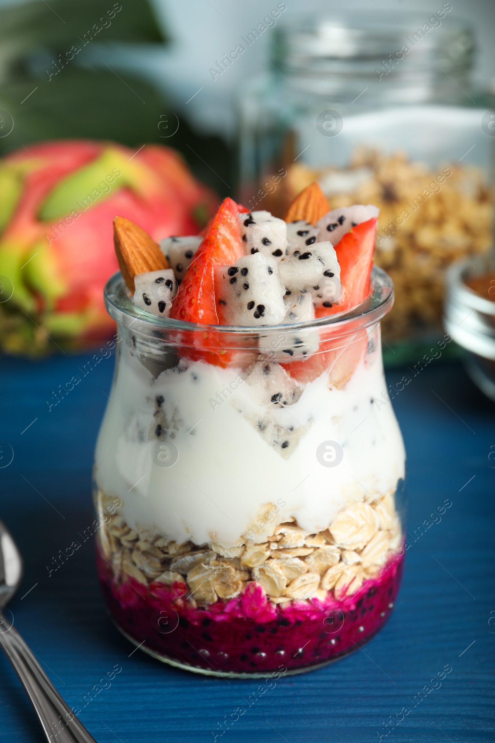 Photo of Glass jar of granola with pitahaya, yogurt and strawberries on blue wooden table