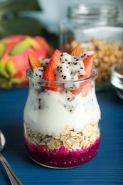 Photo of Glass jar of granola with pitahaya, yogurt and strawberries on blue wooden table