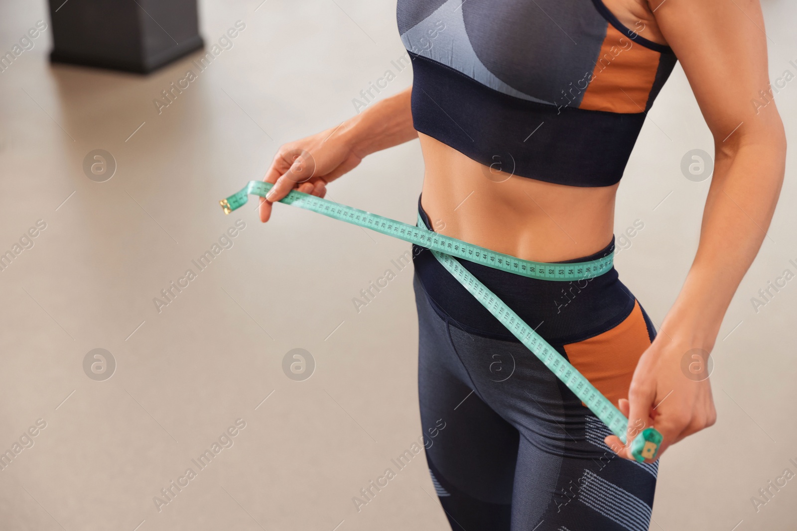 Photo of Slim woman measuring waist with tape in gym, closeup. Space for text