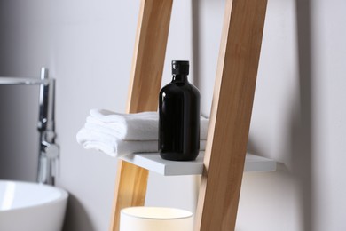 Photo of Bottle of bubble bath and towels on shelf in bathroom