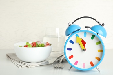 Photo of Alarm clock with salad on white table. Meal timing concept
