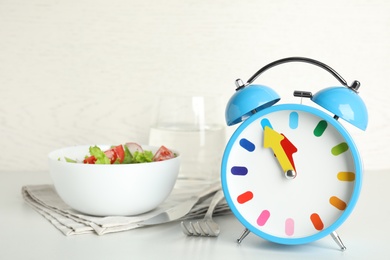 Alarm clock with salad on white table. Meal timing concept