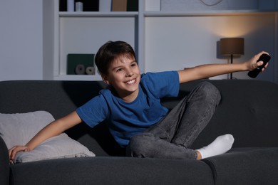 Photo of Happy boy watching TV and holding remote control on sofa at home
