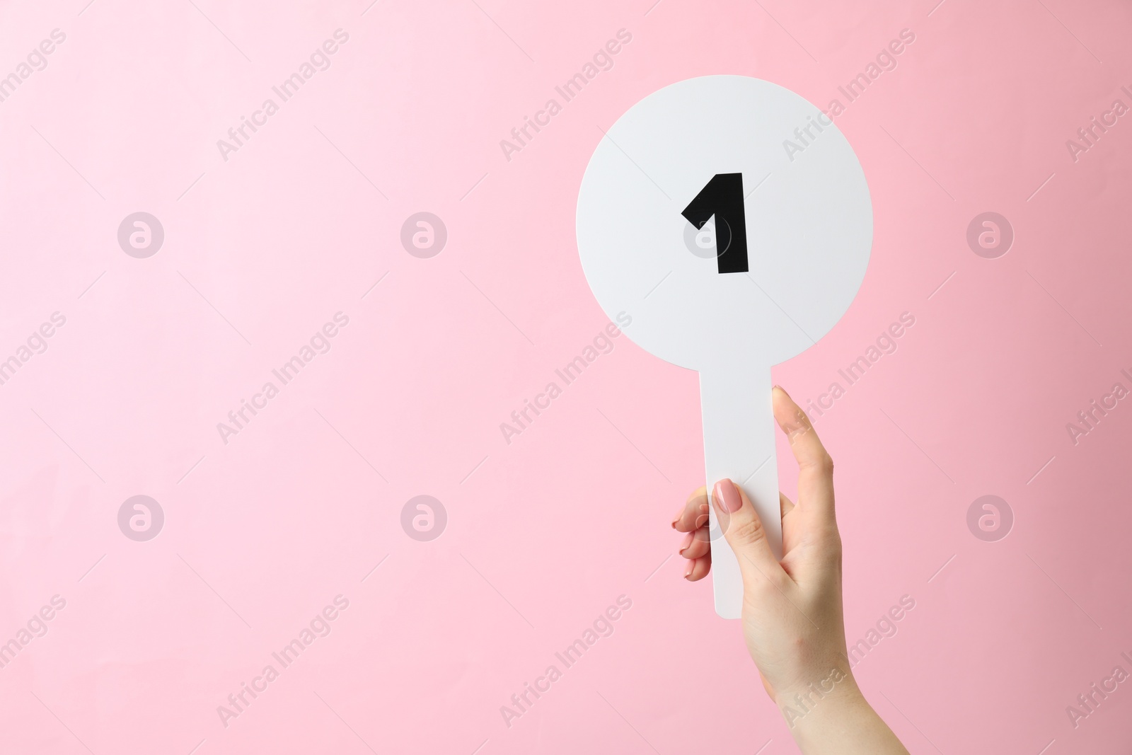 Photo of Woman holding auction paddle with number 1 on pink background, closeup. Space for text