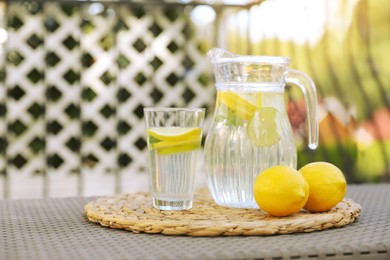 Photo of Glass and jug of water with lemons on table outdoors