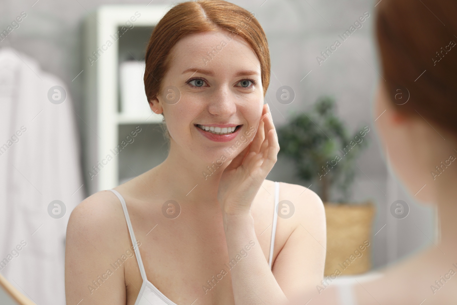 Photo of Smiling woman with freckles near mirror in bathroom