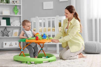 Photo of Mother and her little son at home. Cute baby making first steps with toy walker