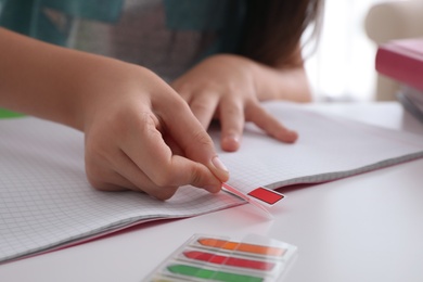 Preteen girl with bookmark and notebook at table, closeup. Doing homework