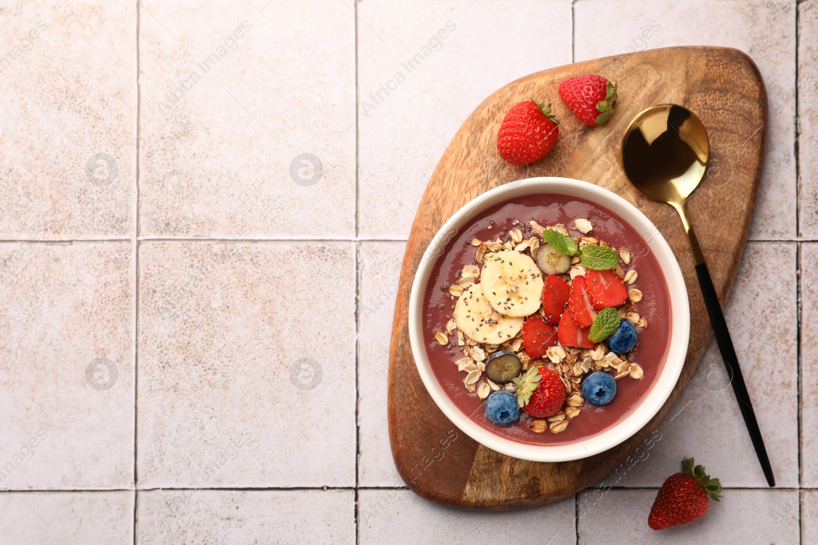 Photo of Delicious smoothie bowl with fresh berries, banana and granola on tiled surface, flat lay. Space for text