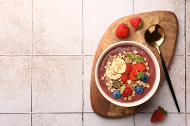 Photo of Delicious smoothie bowl with fresh berries, banana and granola on tiled surface, flat lay. Space for text