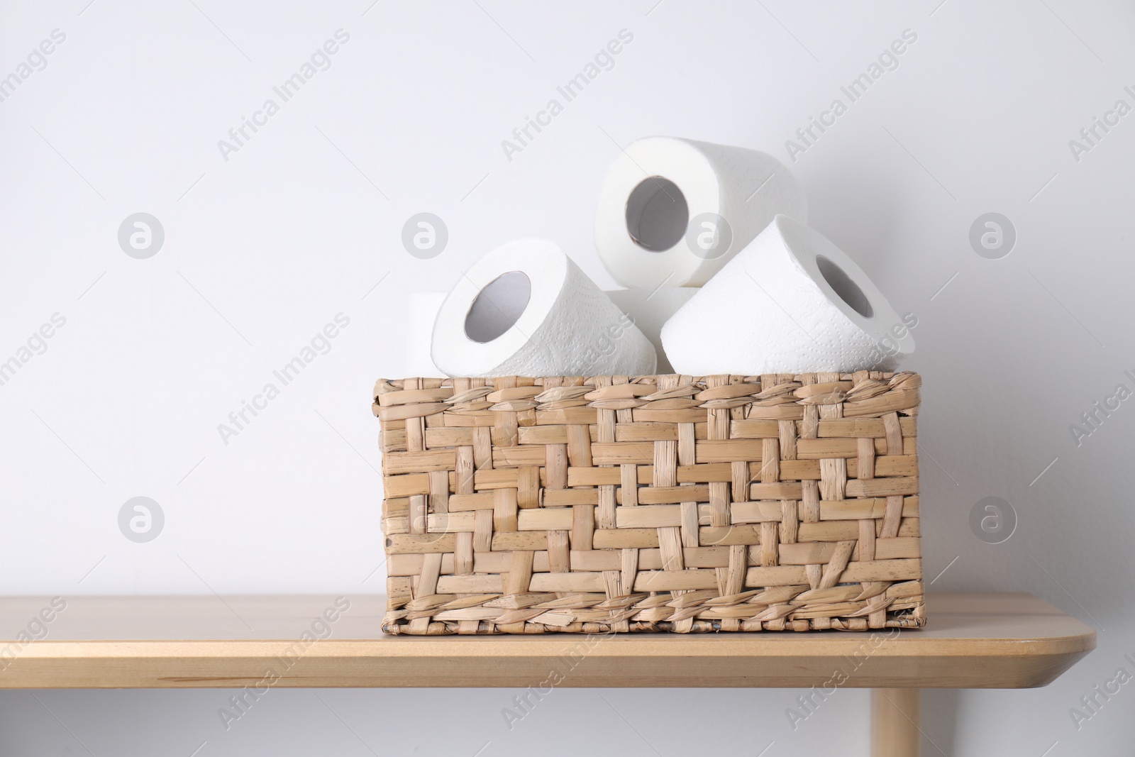 Photo of Toilet paper rolls in wicker basket on wooden table near white wall, space for text