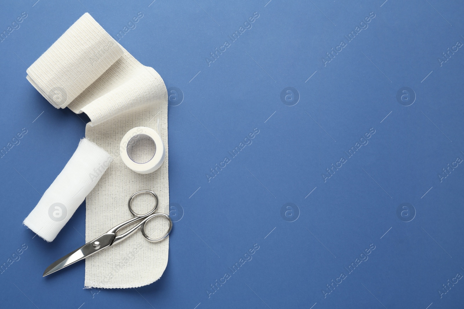 Photo of Medical bandage rolls, sticking plaster and scissors on blue background, flat lay. Space for text