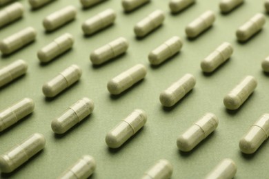 Many vitamin capsules on olive background, closeup