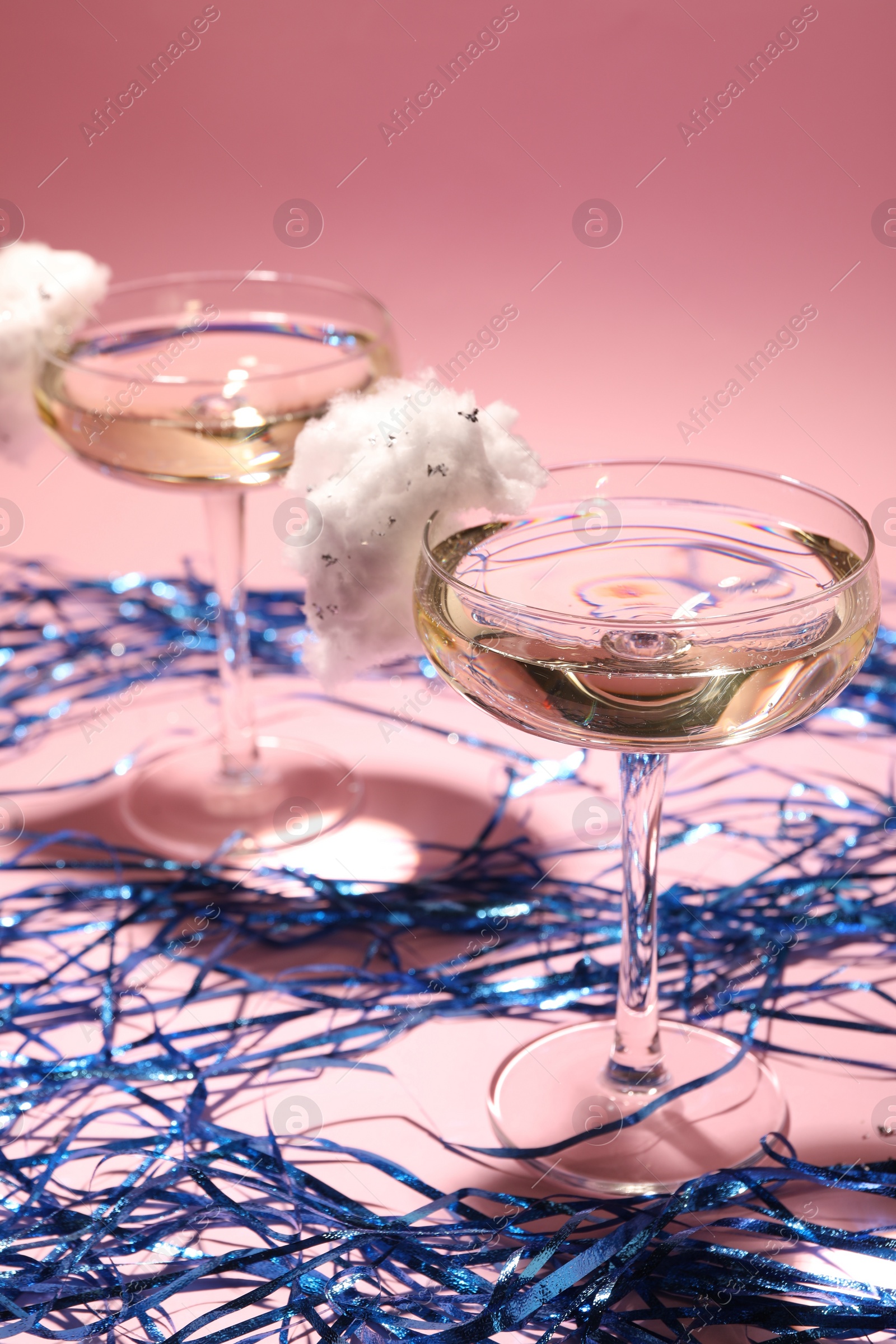 Photo of Tasty cocktails in glasses decorated with cotton candy and blue shiny streamers on pink background