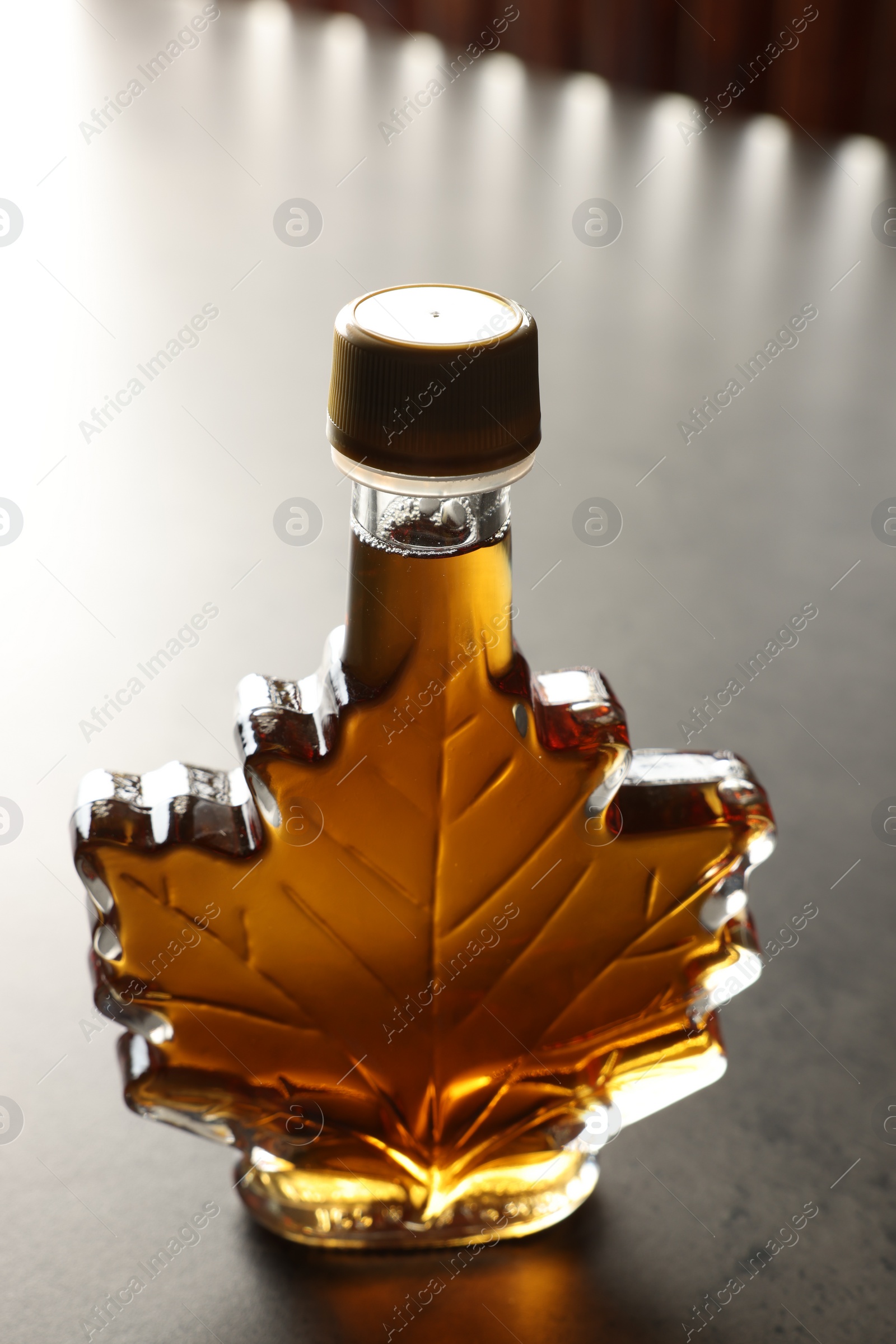 Photo of Leaf shaped bottle of tasty maple syrup on light grey table