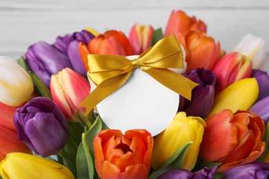 Photo of Bouquet of beautiful colorful tulips with blank card on white wooden background, closeup. Birthday celebration