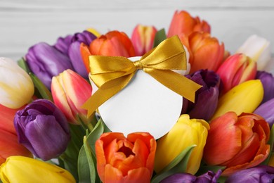 Bouquet of beautiful colorful tulips with blank card on white wooden background, closeup. Birthday celebration