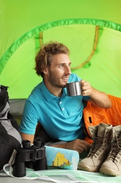 Young man in sleeping bag with mug inside of tent