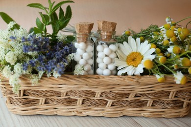 Photo of Bottles with homeopathic remedy and flowers in basket on wooden table, closeup