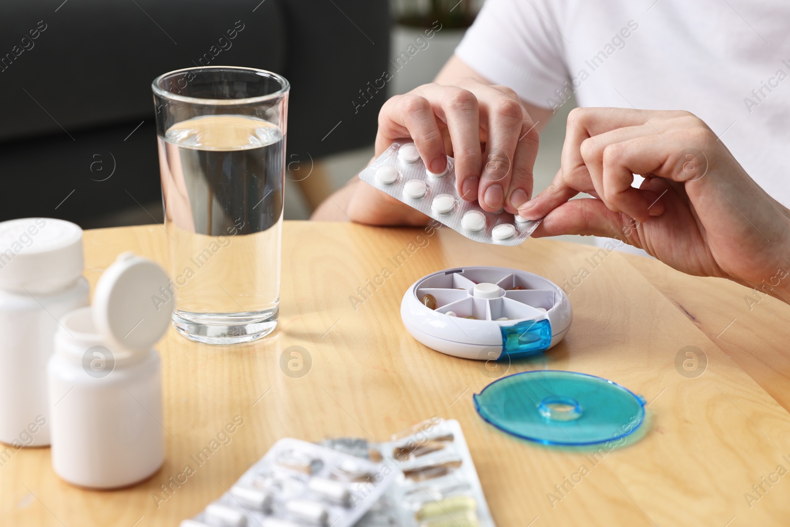 Photo of Woman with pills, organizer and glass of water at light wooden table, closeup