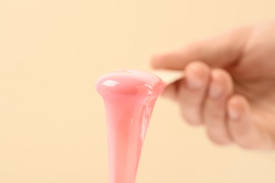 Photo of Woman holding spatula with hot depilatory wax on beige background, closeup