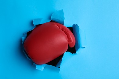 Man breaking through light blue paper with boxing glove, closeup
