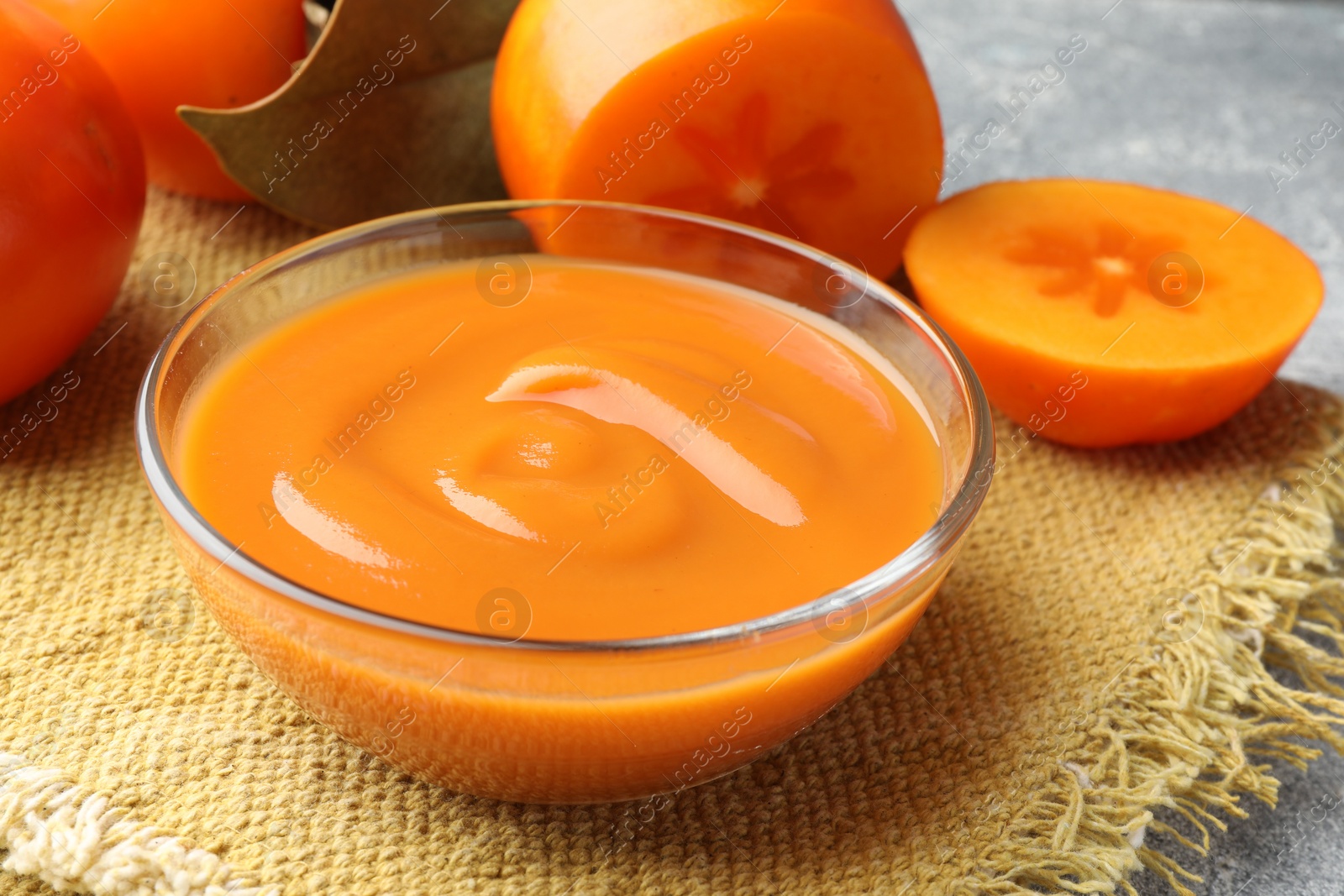 Photo of Delicious persimmon jam in glass bowl and fresh fruits on table, closeup