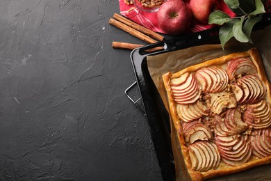 Baking tray with fresh apple galette and fruits on black textured table, flat lay. Space for text