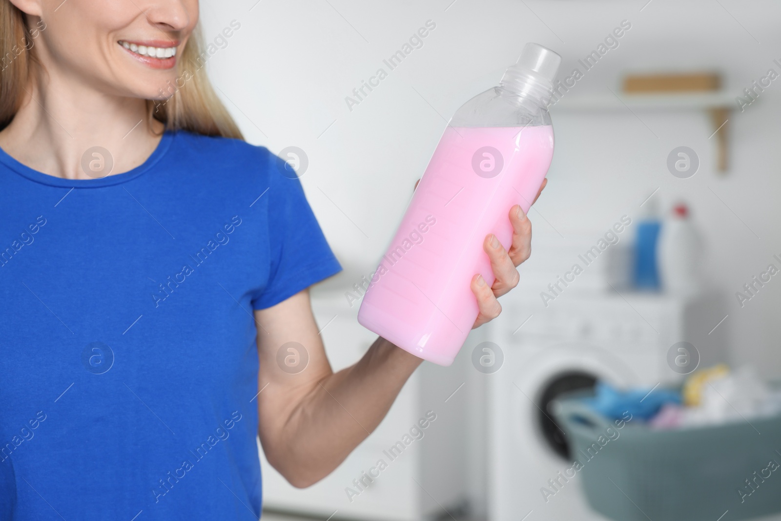 Photo of Woman holding fabric softener in bathroom, closeup. Space for text