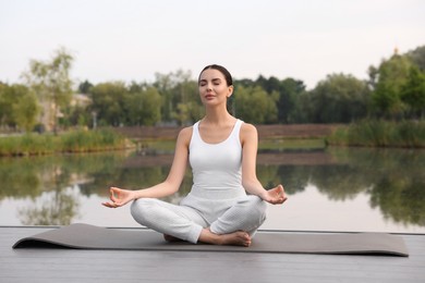 Beautiful young woman practicing Padmasana on yoga mat outdoors. Lotus pose