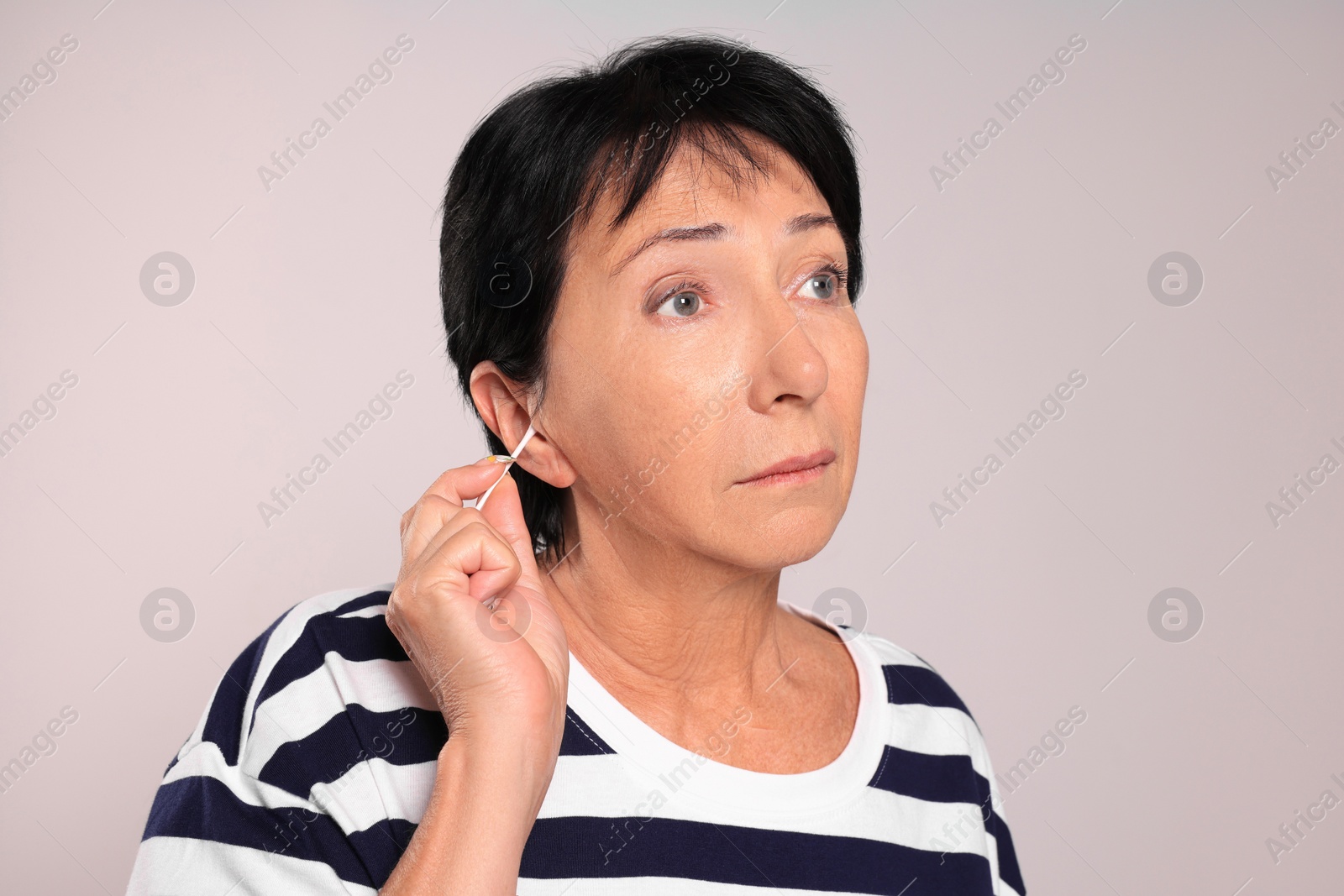 Photo of Senior woman cleaning ear with cotton swab on light grey background