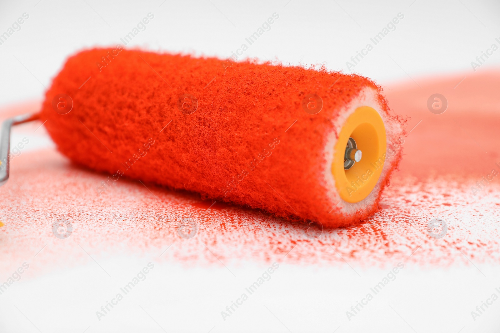 Photo of Roller brush and strokes of orange paint on white background, closeup