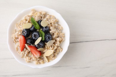 Photo of Tasty oatmeal with strawberries, blueberries and almond petals in bowl on white wooden table, top view. Space for text